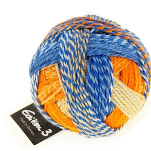 Könnte beinhalten: Eine Garnrolle in den Farben Blau, Orange und Creme. Das Garn besteht aus einer Mischung von Fasern und eignet sich zum Stricken oder Häkeln. Das Etikett auf der Garnrolle lautet "Caelum 3 Made in Germany."