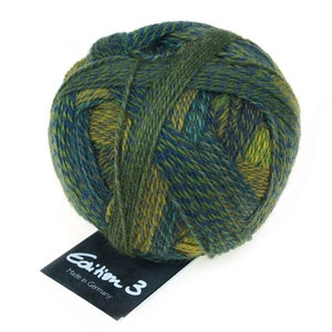 May include: A ball of green, blue and yellow yarn with a black label that reads "Edition 3" and "Made in Germany".