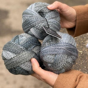 May include: Three balls of yarn in shades of gray and blue. The yarn is a blend of wool and silk.