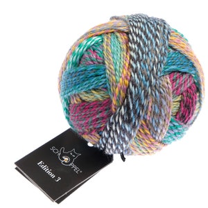 May include: A colorful ball of yarn with a mix of teal, pink, yellow, and gray strands. The yarn is tightly wound, creating a textured surface. A black tag with the text "Edition 3" is attached. Ideal for knitting and crochet projects.