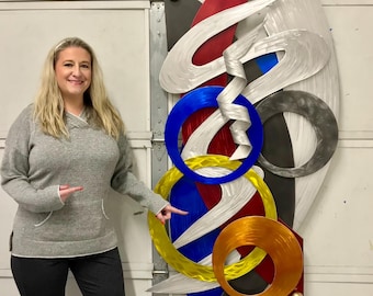 May include: A large abstract metal wall sculpture featuring a variety of shapes and colours, including red, blue, yellow, and silver. The sculpture is made of metal and has a modern, contemporary style.