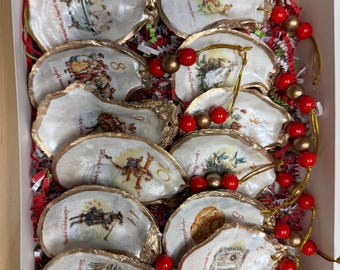 May include: A set of oyster shell ornaments with gold-painted edges, each featuring a different vintage illustration and a number. The ornaments are arranged in a white box with red and green filler, and are strung with red and gold beads.