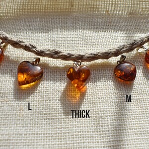 May include: A set of six amber heart pendants of varying sizes, labeled XL, L, Thick, M, S, and XS. The pendants are strung on a natural fiber cord.