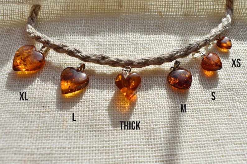 May include: A set of six amber heart pendants of varying sizes, labeled XL, L, Thick, M, S, and XS. The pendants are strung on a natural fiber cord.