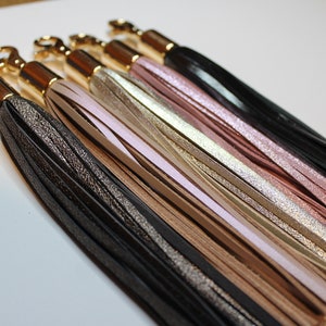 Pu&ograve; includere: Un set di sei portachiavi con anelli in metallo dorato e nappe in pelle di diversi colori. Le nappe sono nere, argentate, beige, rosa chiaro, dorate e rosa.