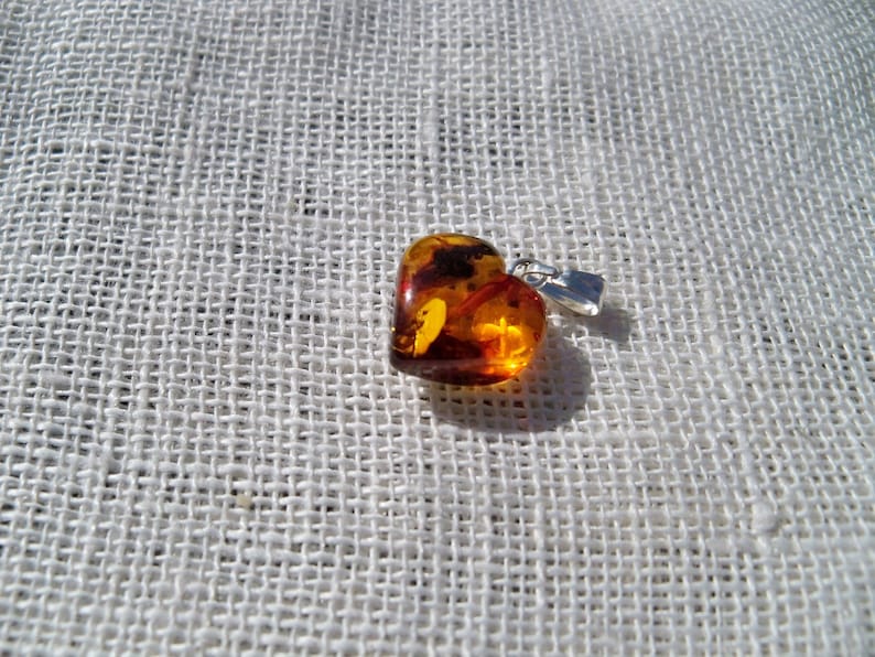 May include: A heart-shaped amber pendant with inclusions, set in silver with a bail for a chain.