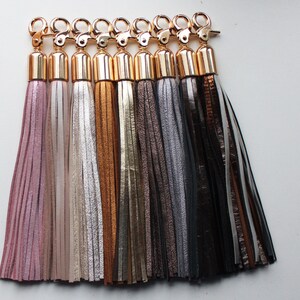 Pu&ograve; includere: Un set di otto portachiavi con nappe in vari colori, tra cui rosa, beige, oro, marrone, grigio e nero. Ogni portachiavi ha un anello metallico dorato e un cappuccio metallico dorato.