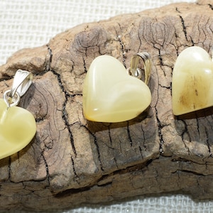 May include: Three heart-shaped pendants made of yellow amber with silver bail. The pendants are displayed on a piece of driftwood.