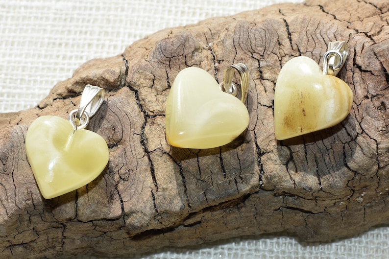 May include: Three heart-shaped pendants made of yellow amber with silver bail. The pendants are displayed on a piece of driftwood.