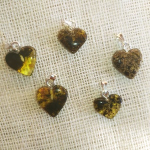 May include: Five heart-shaped amber pendants with silver bail. The amber is a mix of dark brown and yellow with inclusions.