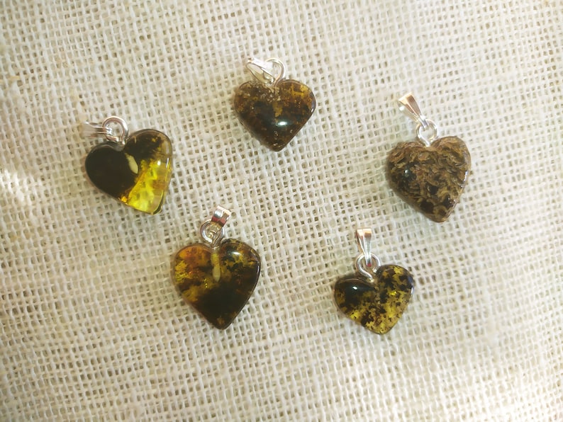 May include: Five heart-shaped amber pendants with silver bail. The amber is a mix of dark brown and yellow with inclusions.