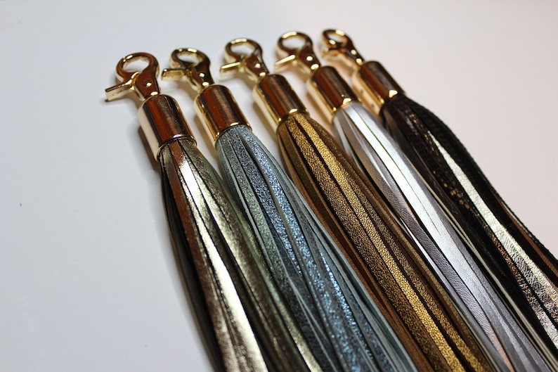 Pu&ograve; includere: Cinque nappine in pelle con chiusure in metallo dorato. Le nappine sono in tonalit&agrave; oro, argento, marrone, bianco e nero.