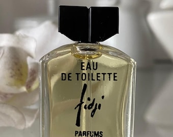 May include: A clear glass bottle of Fidji Eau de Toilette perfume by Guy Laroche Paris. The bottle has a black cap and a label with the brand name and the words "Eau de Toilette".