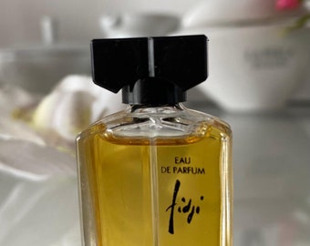 May include: A small, clear glass bottle of Fiji Eau de Parfum by Guy Laroche Paris. The bottle has a black cap and a gold label with the text "Eau de Parfum Fiji" and "Parfums Guy Laroche Paris 5 ml 88% vol".