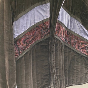 May include: A black quilted jacket with blue and paisley patterned fabric accents. The jacket has a zip closure and a collar.