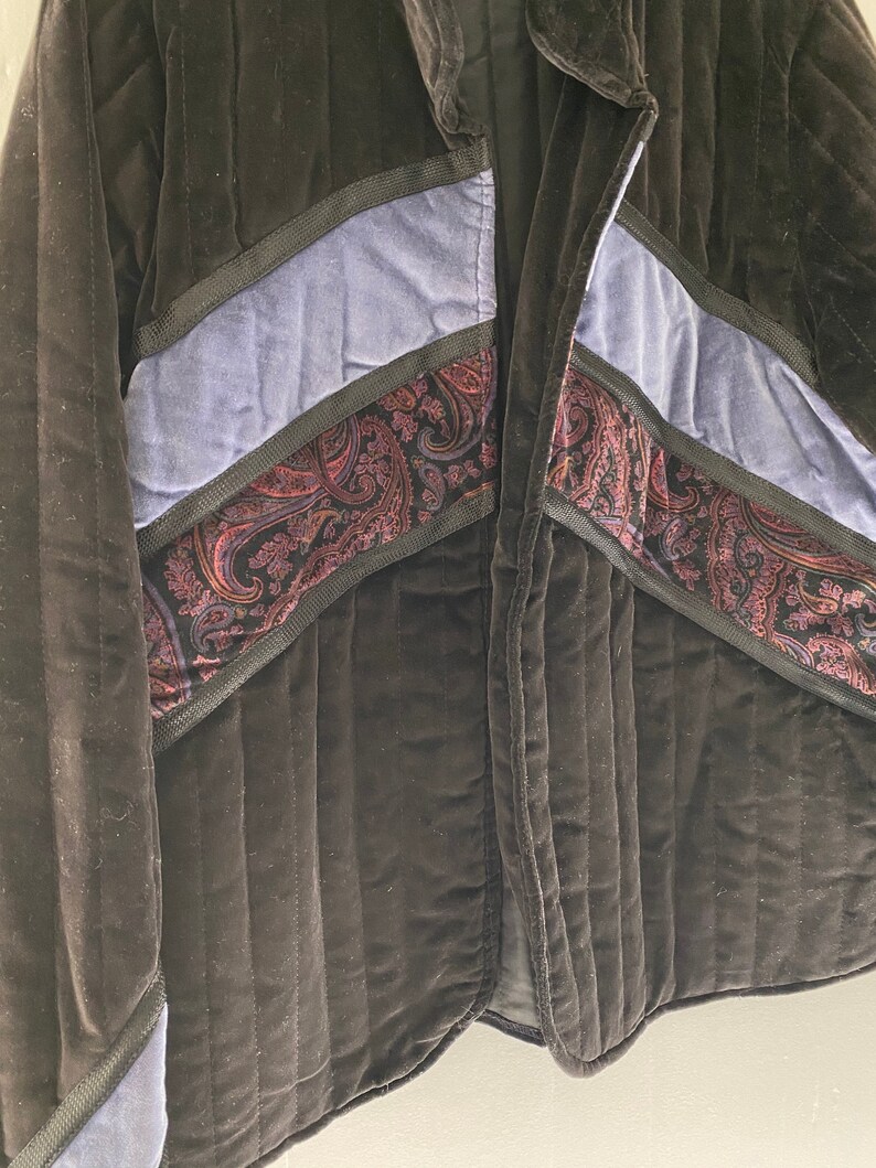 May include: A black quilted jacket with blue and paisley patterned fabric accents. The jacket has a zip closure and a collar.
