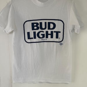 May include: White t-shirt with a blue Bud Light logo. The logo is a rectangle with the words "Bud Light" in a bold, blue font. The words "Beer" are printed in smaller, blue font below the logo.