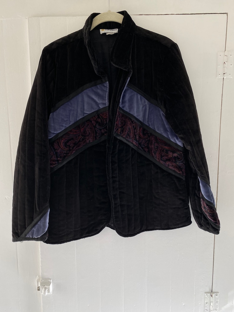 May include: A black quilted jacket with a paisley pattern and blue and burgundy accents. The jacket has a zip closure and a collar.