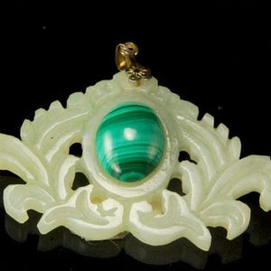 Puede incluir: Un colgante de jade blanco tallado con una piedra de malaquita verde engastada en el centro. El colgante presenta un diseño floral y una anilla de oro.