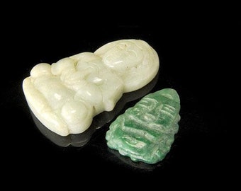 May include: Two jade carvings, one white and one green. The white carving is of a seated figure with a serene expression. The green carving is of a stylized face with intricate details.