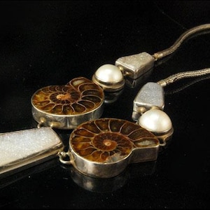 Puede incluir: Un collar de plata con dos fósiles de amonites marrones, perlas blancas y piedras de ágata blancas.