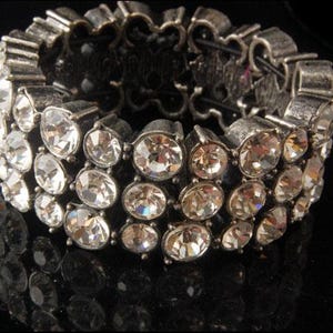 Op de afbeelding: Een zilveren armband met meerdere rijen heldere strass steentjes. De armband is gemaakt van metaal en heeft een decoratief ontwerp.