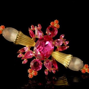 Op de afbeelding: Een broche van roze en koraalkleurige strass met een grote roze middelste steen en gouden accenten.