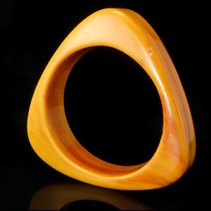 May include: A vintage, triangular-shaped bangle bracelet. The bracelet is a warm amber color with variations in tone, creating a marbled effect. The smooth, polished surface reflects light, highlighting its unique form. A classic jewelry piece.