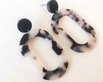 May include: A pair of oval-shaped earrings with a black and white tortoiseshell pattern. The earrings have a black disc at the top and a silver post.