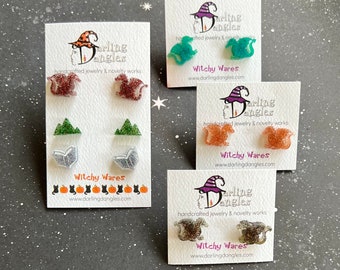 May include: Four sets of earrings featuring various designs, including squirrels, mountains, and books. Each set is displayed on a white card with the text "Darling Dangles" and "Witchy Wares" along with a website address.