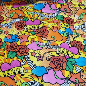 May include: A colorful fabric with a repeating pattern of hearts, stars, roses, and musical notes. The background is yellow with orange, pink, blue, and green accents. The words "LOVE" are repeated throughout the pattern.