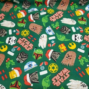 May include: Green fabric with a repeating pattern of Star Wars characters and symbols. The characters include Darth Vader, Chewbacca, Yoda, R2-D2, and Boba Fett. The symbols include the Star Wars logo, the Death Star, and the Millennium Falcon. The fabric is decorated with holly and presents, giving it a festive Christmas feel.