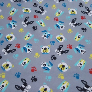 May include: A gray fabric featuring a repeating pattern of stylized dog faces in white, black, yellow, and blue, interspersed with small paw prints in red, yellow, black, and light blue. The text www.snappybaby.etsy.com is printed in the corner.
