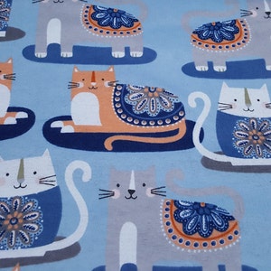 May include: A blue fabric with a repeating pattern of cats wearing colorful patterned clothing. The cats are in various poses, some sitting, some lying down, and some standing. The fabric has a light blue background.