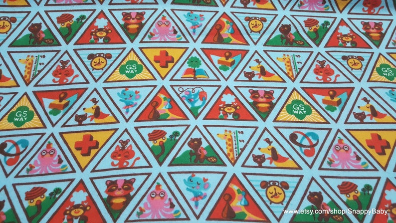 Puede incluir: Una tela azul con un patr&oacute;n repetido de tri&aacute;ngulos marrones. Cada tri&aacute;ngulo contiene una ilustraci&oacute;n colorida diferente, incluyendo una jirafa, un gato, un perro, un libro, una cruz de primeros auxilios, un reloj y un pulpo. El texto "GS WAY" aparece en varios de los tri&aacute;ngulos.