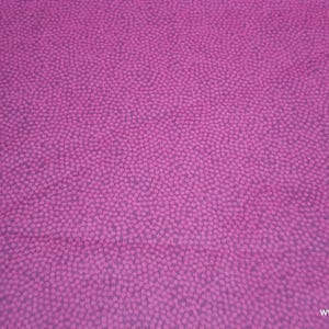 May include: A close-up of a pink fabric with a subtle pattern of small, white dots.
