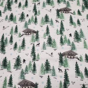 May include: White fabric with a repeating pattern of green pine trees, brown houses, deer, and a Bigfoot-like creature. The background is a light cream color with small blue snowflakes.