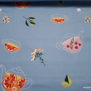 May include: A blue fabric with a repeating pattern of teapots, teacups, and flowers. The teapots and teacups are filled with orange citrus slices and pink berries. The flowers are white with yellow centers.