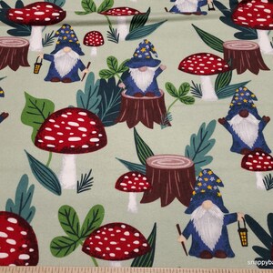 May include: A green fabric with a repeating pattern of gnomes wearing blue hats and holding lanterns, red and white mushrooms, and green leaves.
