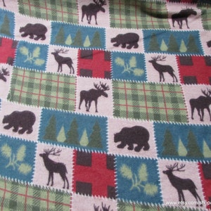 May include: A fabric featuring a repeating patchwork pattern of squares. The design includes dark brown silhouettes of moose, bears, and deer, alongside green pine trees, pine cones, and red and green plaid squares on a light beige background.