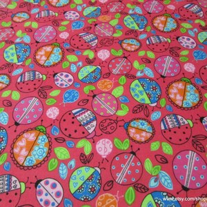 May include: A pink fabric with a repeating pattern of colorful ladybugs with black outlines. The ladybugs have different patterns and colors, including pink, blue, green, orange, and white. The background is a solid pink color.