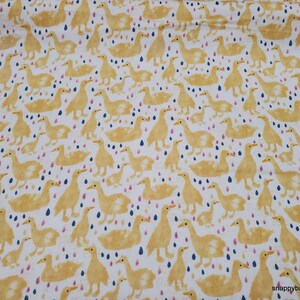 May include: A white fabric with a repeating pattern of yellow ducks and blue and pink raindrops. The ducks are in various poses, some with their heads up and some with their heads down. The raindrops are scattered throughout the fabric.