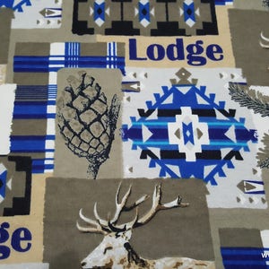 May include: Fabric featuring a repeating pattern of deer, pinecones, pine branches, and geometric shapes in shades of blue, black, white, and tan. The word Lodge is printed in blue text throughout the design, which also includes blue plaid sections.