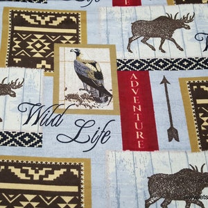 May include: A blue and white fabric with a repeating pattern of moose, eagles, arrows, and geometric designs. The fabric features the text "Wild Life" and "Adventure".