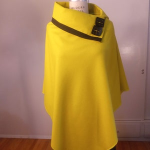 May include: A bright yellow poncho with a black trim and two black buttons on the collar. The poncho is made of a soft, comfortable fabric and has a relaxed fit.
