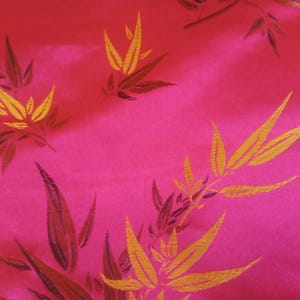May include: A vibrant pink fabric with a repeating pattern of stylized bamboo leaves. The leaves are primarily gold with dark brown accents, creating a striking contrast against the bright pink background. The fabric has a subtle sheen.