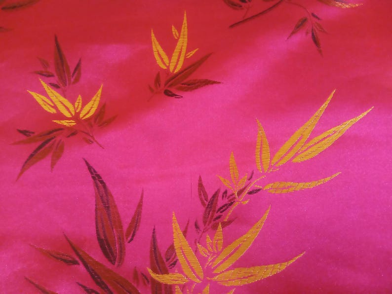 May include: A vibrant pink fabric with a repeating pattern of stylized bamboo leaves. The leaves are primarily gold with dark brown accents, creating a striking contrast against the bright pink background. The fabric has a subtle sheen.