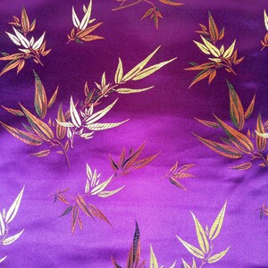 May include: Close-up of a vibrant purple fabric with a repeating pattern of stylized bamboo leaves. The leaves are rendered in shades of gold, white, orange, and green, creating a rich, textured appearance. The fabric has a subtle sheen, enhancing the visual depth.