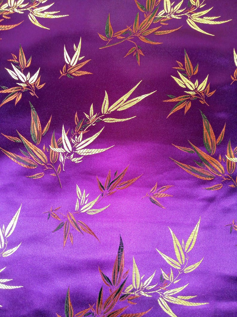 May include: Close-up of a vibrant purple fabric with a repeating pattern of stylized bamboo leaves. The leaves are rendered in shades of gold, white, orange, and green, creating a rich, textured appearance. The fabric has a subtle sheen, enhancing the visual depth.