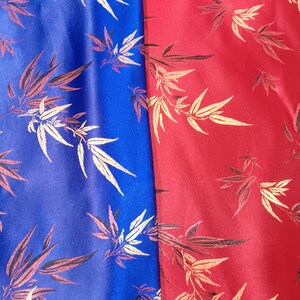 May include: Close-up of two fabric panels, one blue and one red. Both panels feature a repeating pattern of bamboo leaves in gold and brown. The fabric has a slight sheen, suggesting a satin or silk material.